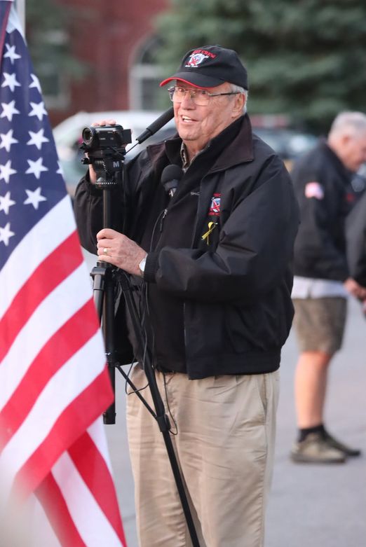 volunteer beside the American flag at an Honor Flight send-off ceremony
